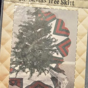 May include: A Patch Press Christmas Tree Skirt sewing pattern package featuring a quilted tree skirt with red, green, and white heart-shaped patchwork designs. The packaging includes text, a graphic of a decorated tree, and a small white kitten.