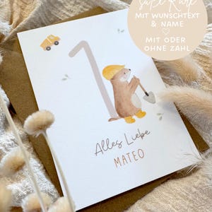 Könnte beinhalten: Eine weiße Grußkarte mit der Zahl Eins, einem braunen Otter mit gelbem Bauhelm und Stiefeln, der eine Schaufel hält, einem kleinen gelben LKW und dem Text Alles Liebe MATEO. Ein beiger Kreis enthält den Text süße Karte MIT WUNSCHTEXT & NAME MIT ODER OHNE ZAHL.