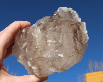 May include: A large, clear quartz crystal with a smoky brown hue. The crystal has a rough, natural texture and is irregularly shaped.