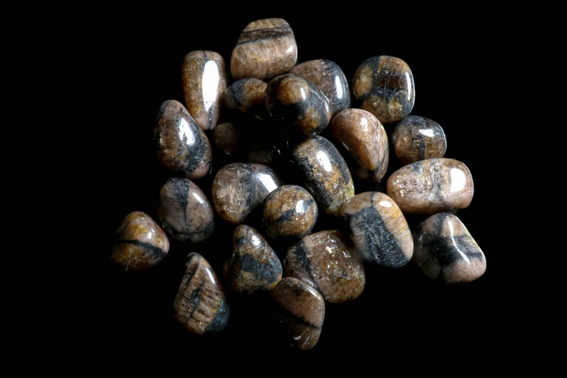 Puede incluir: Una colecci&oacute;n de piedras marrones y negras pulidas con un patr&oacute;n estriado. Las piedras son lisas y pulidas.