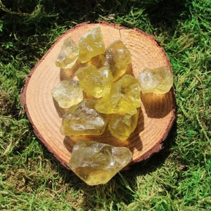 May include: A collection of yellow citrine crystals on a wooden surface. The crystals are various sizes and shapes, with some having a more pointed shape and others being more rounded.