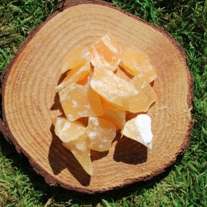 May include: A collection of orange calcite crystals on a wooden surface. The crystals are various sizes and shapes, with some having a translucent appearance.