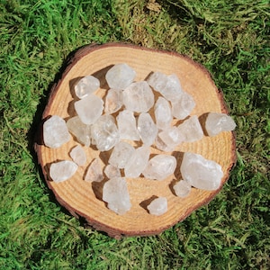 May include: A collection of clear quartz crystals of various sizes and shapes, displayed on a wooden surface. The crystals are arranged in a cluster, with some overlapping.