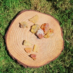 May include: A collection of amber stones of various shapes and sizes, displayed on a wooden surface. The stones are a mix of yellow and orange hues.