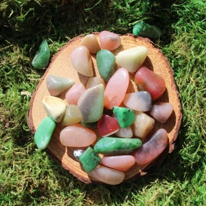 May include: A collection of smooth, polished stones in various shades of green, pink, and white. The stones are arranged on a wooden surface, creating a visually appealing display.