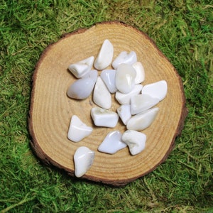 May include: A collection of white and light blue agate tumbled stones on a wooden surface. The stones are smooth and polished, and they have a variety of shapes and sizes.
