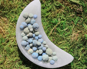 May include: A white crescent moon-shaped dish filled with blue and green gemstone beads.