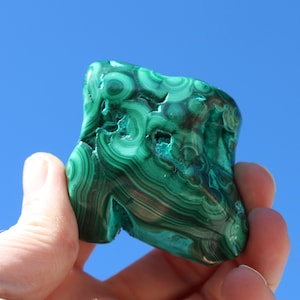 May include: A green malachite stone with a swirling pattern. The stone is smooth and polished.