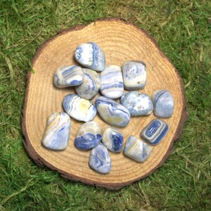 May include: A collection of blue and white banded agate tumbled stones on a wooden surface. The stones are smooth and polished, with a variety of patterns and colors.