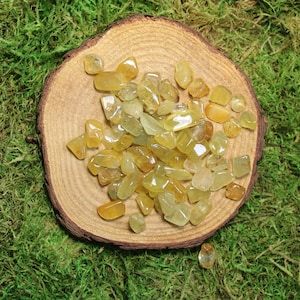 May include: A collection of yellow citrine tumbled stones on a wooden surface. The stones are smooth and polished, with a variety of shapes and sizes.