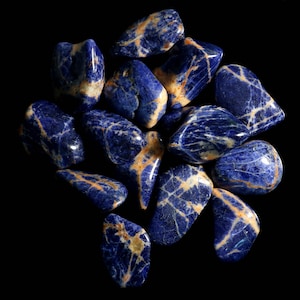 May include: A collection of tumbled blue and white sodalite stones. The stones are smooth and polished, with a variety of shapes and sizes.