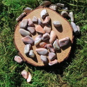 May include: A collection of agate stones in various shades of pink, white, and gray. The stones are arranged on a wooden slice and have a natural, polished finish.