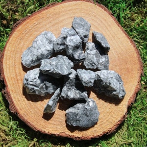 May include: A collection of gray and white tumbled stones on a wooden surface. The stones are rough and have a natural, organic look.