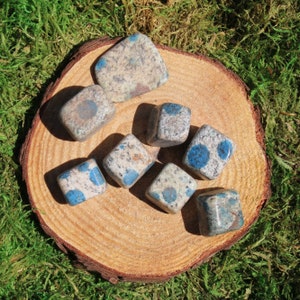 May include: A collection of eight blue and white polished stones with a speckled pattern. The stones are arranged on a wooden surface.