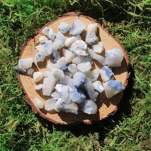 May include: A collection of white and blue crystal chips with a blue-grey tint. The chips are arranged on a wooden surface.