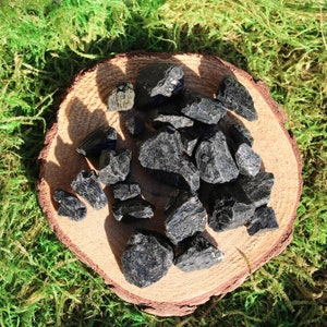 May include: A collection of black tourmaline crystals on a wooden surface. The crystals are rough and have a natural, unpolished look.