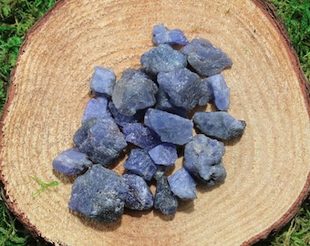 May include: A collection of blue-purple tumbled stones on a wooden surface. The stones are various sizes and shapes, with a rough, natural texture.