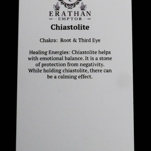 Puede incluir: Una tarjeta blanca con texto negro que describe las propiedades curativas de la chiastolite. La tarjeta tiene el texto "ERATHAN EMPTOR" y "Chiastolite" en la parte superior. El texto dice "Chakra: Ra&iacute;z y Tercer Ojo" y "Energ&iacute;as curativas: La chiastolite ayuda con el equilibrio emocional. Es una piedra de protecci&oacute;n contra la negatividad. Mientras se sostiene la chiastolite, puede haber un efecto calmante." La tarjeta tambi&eacute;n tiene la direcci&oacute;n del sitio web "www.erathanemptor.com" en la parte inferior.