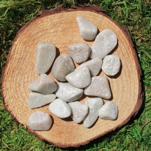 May include: A collection of white and gray tumbled stones on a wooden surface. The stones are smooth and have a natural, polished look.