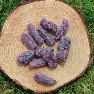 May include: A collection of purple amethyst crystal points on a wooden surface. The crystals are various sizes and shapes, with some being long and thin, while others are shorter and wider.