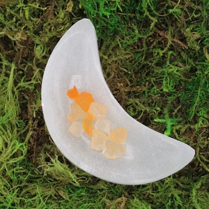 May include: A white crescent moon-shaped dish filled with small orange and yellow crystals.