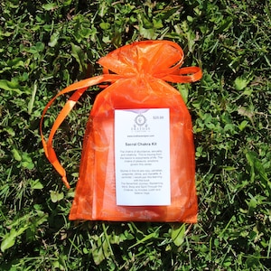 May include: An orange organza bag with a white label that reads "Sacral Chakra Kit" and includes information about the chakra and the stones in the kit. The label also includes the price of $25.00.