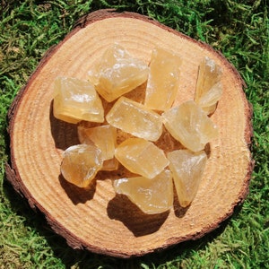 May include: A collection of raw, honey-colored calcite crystals on a wooden surface. The crystals are various sizes and shapes, with some having a translucent appearance.