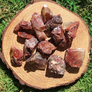 May include: A collection of red and brown gemstone crystals with a translucent quality. The crystals are arranged on a wooden surface.