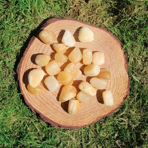 May include: A collection of tumbled citrine stones in various sizes and shades of yellow and orange, displayed on a wooden surface.