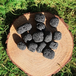 May include: A collection of small, black, porous lava rocks on a wooden surface. The rocks are irregularly shaped and have a rough texture.