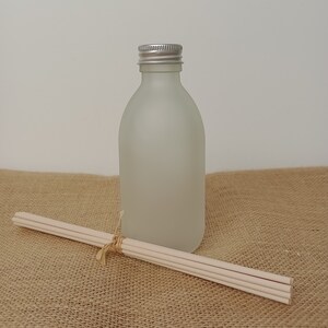 May include: A frosted glass bottle with a silver lid and a bundle of wooden diffuser sticks. The bottle and sticks are on a brown hessian surface.
