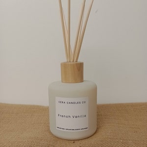 May include: A white frosted glass diffuser bottle with a wooden lid and natural reeds. The bottle has a label that reads "Cera Candles Co. French Vanilla 100% Soy Wax 100% Natural Scents 100% Vegan".