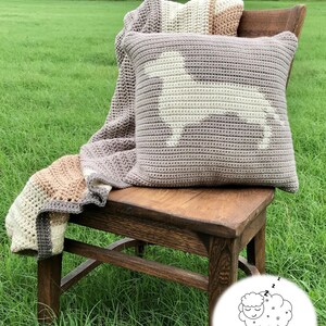 May include: A crocheted pillow with a white dog silhouette on a light brown background. The pillow is sitting on a wooden chair with a crocheted blanket draped over the back. The chair is on a grassy lawn.