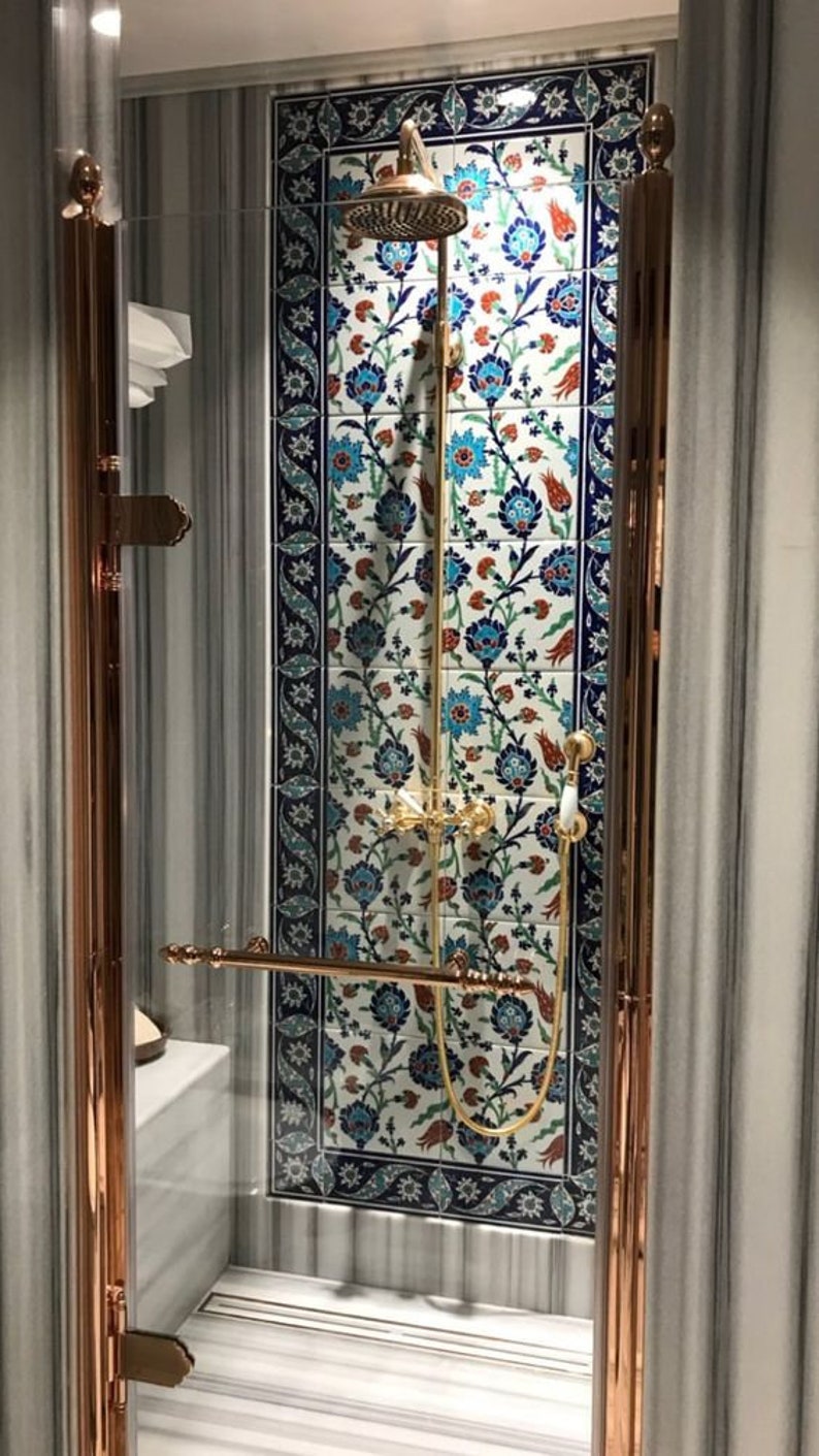 Pode incluir: Um box de chuveiro com uma porta de vidro e acess&oacute;rios dourados. O chuveiro &eacute; de design circular com acabamento dourado. O box de chuveiro &eacute; revestido com azulejos brancos com um padr&atilde;o floral azul e vermelho.