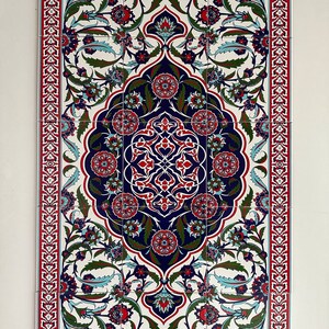 May include: A white ceramic tile with a red, blue, and green floral pattern. The tile is part of a larger design that resembles a traditional Turkish rug.