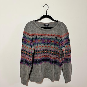 May include: Gray sweater with a colorful geometric pattern. The sweater has long sleeves and a crew neck. The brand label reads "Chaps".