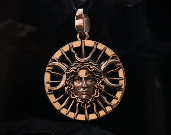May include: A gold-toned pendant necklace featuring a circular design with a woman's face surrounded by a sunburst and crescent moons.