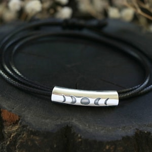 May include: A black leather bracelet with a silver charm featuring a crescent moon design.