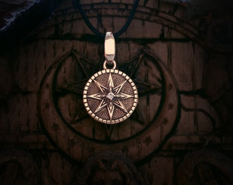 May include: A silver pendant with a starburst design and a small diamond in the center. The pendant is hanging from a black cord.