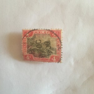 Puede incluir: Un sello postal vintage de los Estados Malayos Federados. El sello tiene un borde rojo y presenta una ilustración detallada de un tigre. El texto incluye "MALAY STATES" y "POSTAGE REVENUE".