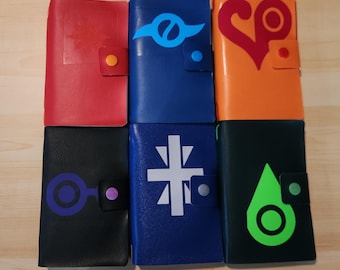 May include: Six rectangular leather-like journals arranged in two rows of three. The covers are red, blue, orange, black, dark blue, and dark green, each featuring a unique graphic symbol and a matching colored snap button closure on the side.