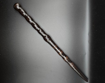 May include: A dark brown wooden wand with a twisted design. The wand is about 12 inches long and has a pointed tip.