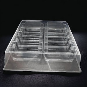 May include: Clear plastic tray with multiple compartments. The tray is rectangular with a series of stepped levels and dividers, designed for organizing small items. The transparent material allows for easy visibility of the contents.