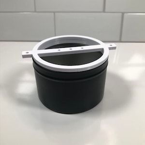 May include: A white plastic ring with a black base and a white bar across the top. The ring has five holes in it.