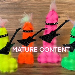 May include: Four colourful, phallic-shaped objects with black glitter guitars and black studded belts. The objects are made of a textured material and have a fuzzy, pink, blue, or green top. The background is a wood grain surface.  MATURE CONTENT