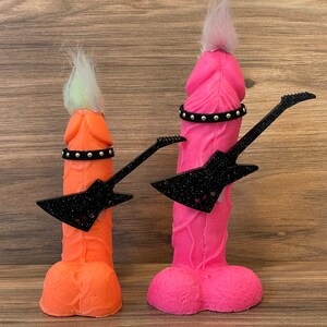 May include: Two colourful, anthropomorphic figures with hair and a black guitar. The figure on the left is orange and the figure on the right is pink.