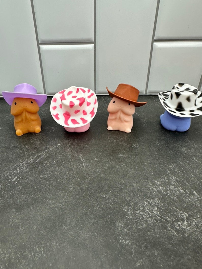 Puede incluir: Cuatro figuras novedosas, cada una con un sombrero de vaquero &uacute;nico. Los sombreros son morados, rosas con lunares blancos, marrones y con estampado de vaca en blanco y negro. Las figuras son de varios tonos de piel y azules.