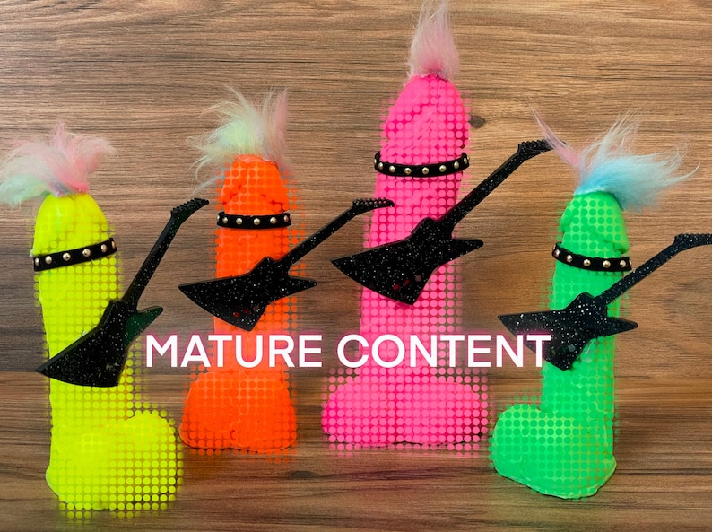 May include: Four colourful, phallic-shaped objects with black glitter guitars and black studded belts. The objects are made of a textured material and have a fuzzy, pink, blue, or green top. The background is a wood grain surface.  MATURE CONTENT