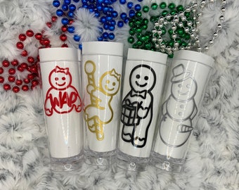 Op de afbeelding: Vier witte plastic bekers met transparante bodems, elk met een ander peperkoekthema-ontwerp in rood, goud, zwart en zilver. De ontwerpen omvatten een peperkoekman met het woord "WAR", een peperkoekpersoon met een zuurstok, een peperkoekman met een cadeau en een sneeuwpop.