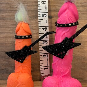 May include: Two novelty figures, one pink and one orange, each holding a black glitter guitar and wearing a studded belt. The figures are approximately 5 inches tall.